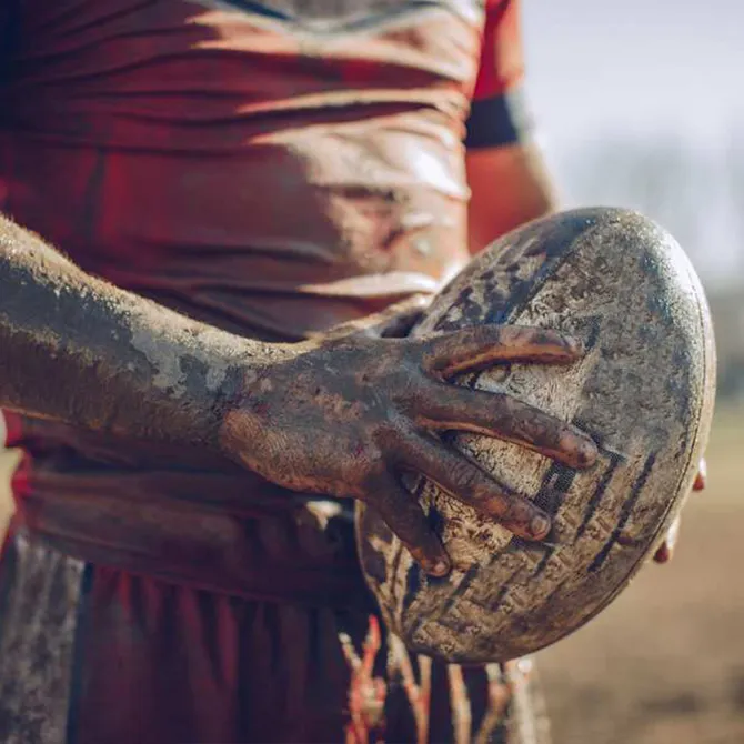 Close up of a muddy rugby player holding a rugby ball