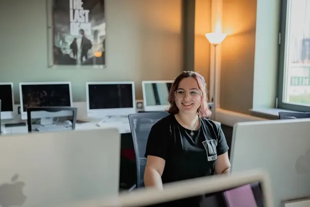 Film student, Amy, smiles at the camera whilst sat at a desk with computers