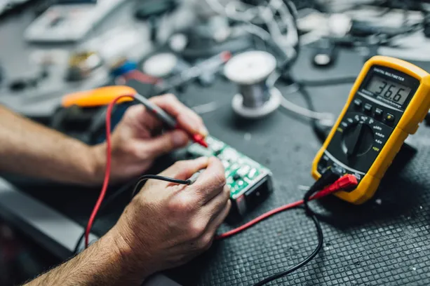 Closeup of hands checking board with multimeter