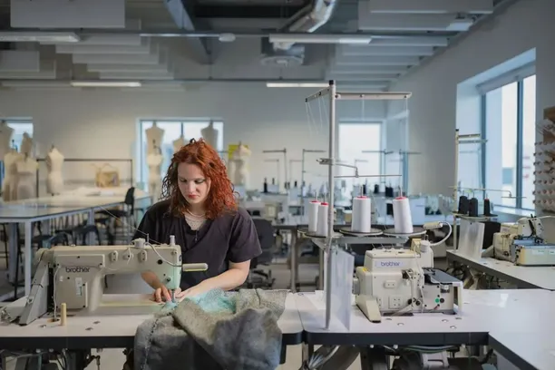 Fashion student sitting at a desk using a sewing machine.