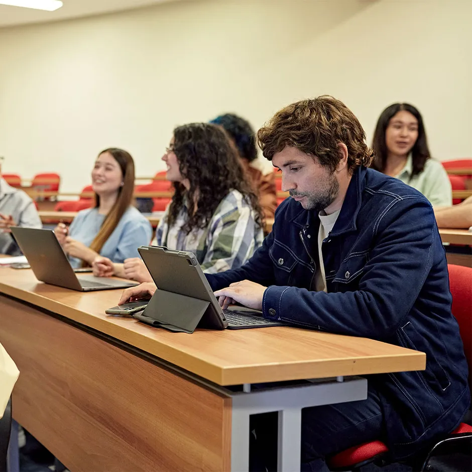 students sitting at a lecture theatre table typing on laptops while listening in class