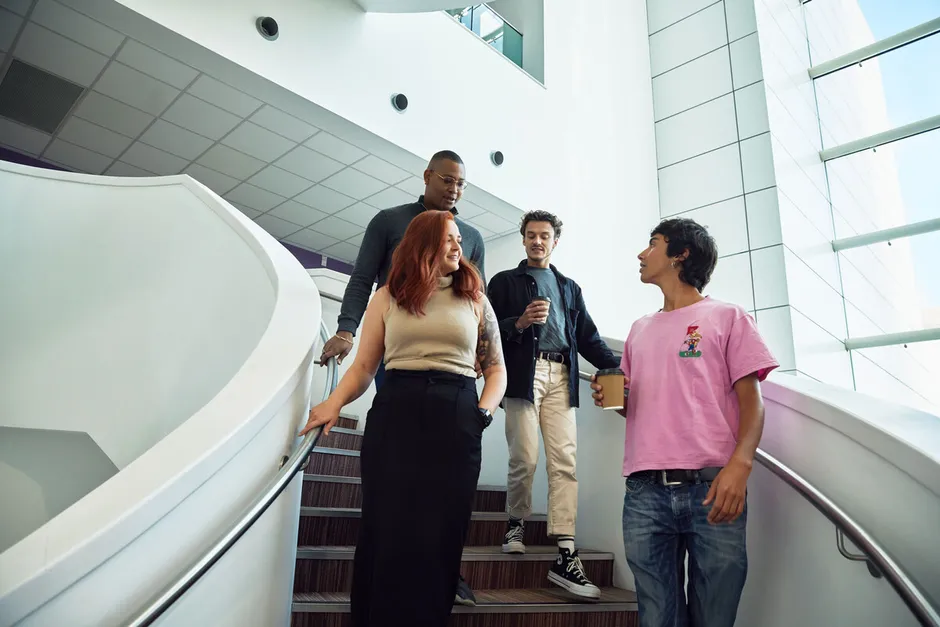 Four students walking down a spiral staircase and talking to eachother.
