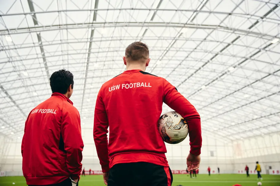 Two football coaching students looking out onto a indoor football pitch.