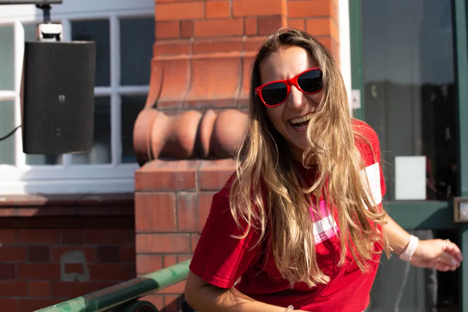 A student ambassador, wearing red USW sunglasses and a branded tshirt, dancing outside at the Glyntaff campus.
