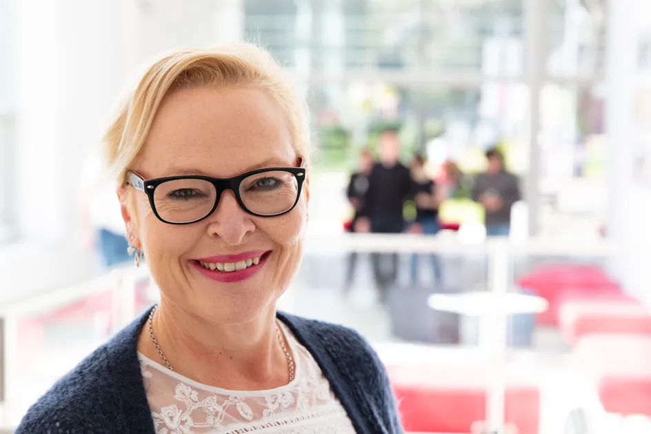 Professor Deborah Lancastle smiles at the camera in the Treforest psychology building foyer with students in the background
