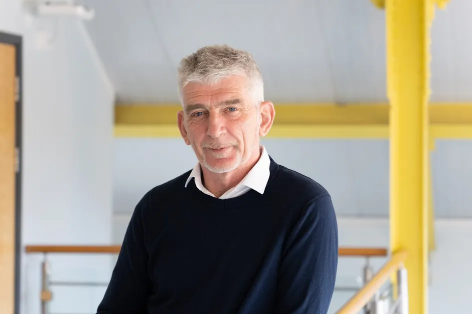 Professor Stuart Todd looks at the camera from an indoor balcony with white walls and yellow beams in the background