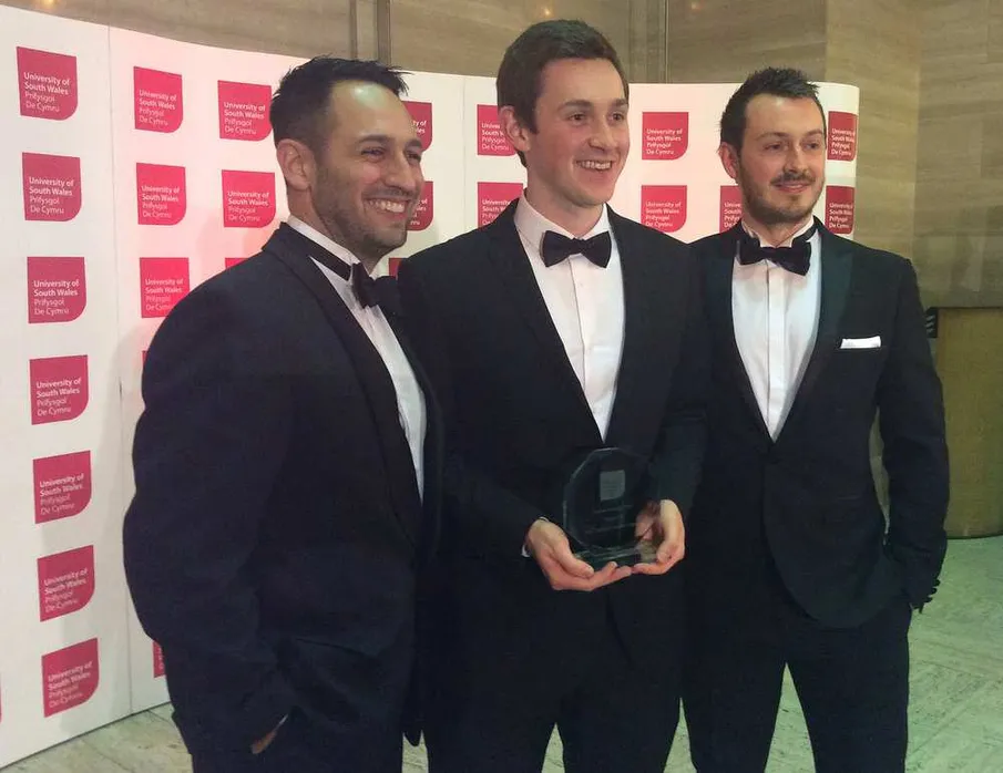 Three men in suits holding an award in front of a USW backdrop