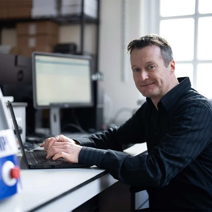 Associate Professor Tim Patterson looks at the camera while sat at a desk and typing on a laptop
