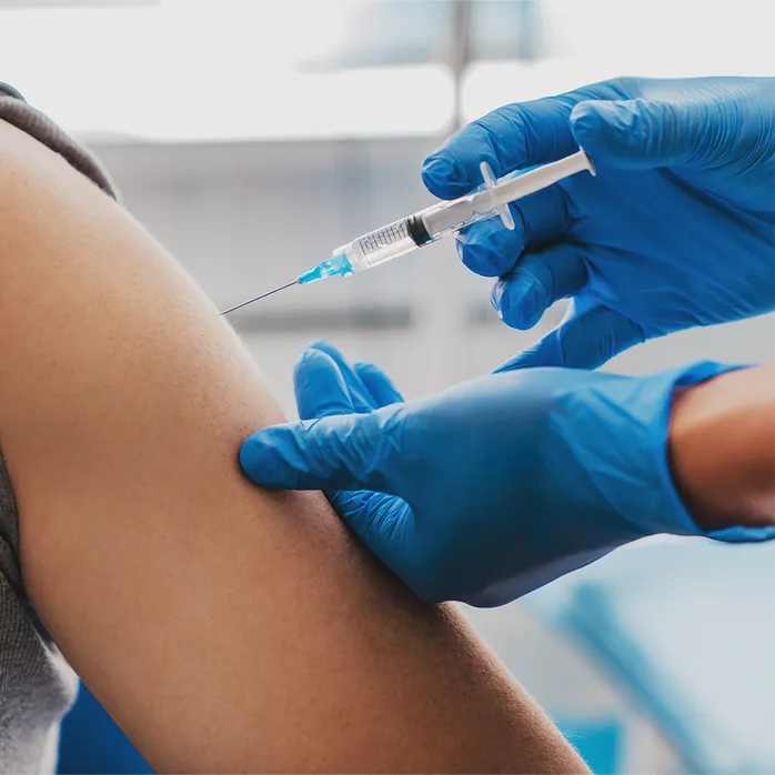 A medical professional in blue gloves administers an injection into a patient's arm