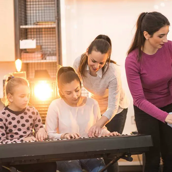 Dau athro cerdd yn arwain dau fyfyriwr i ganu'r piano