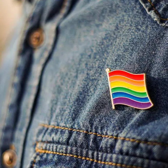 A close up of a rainbow flag badge pinned onto a denim jacket