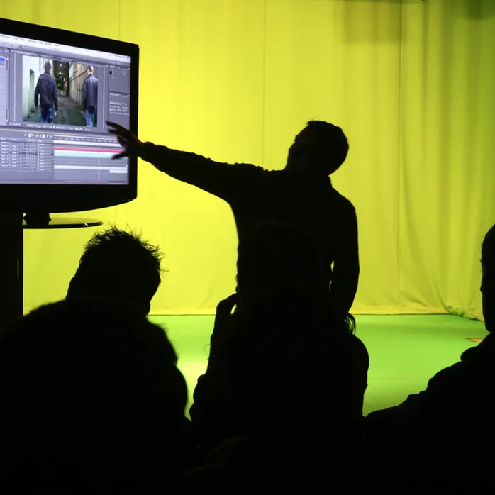 A silhouette of a lecturer pointing at editing software, in a green room at Cardiff campus