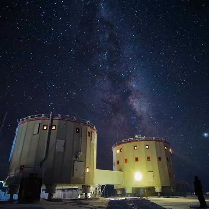 Dyn yn gorwedd mewn sganiwr MRI a grŵp o bobl yn gwenu ar y camera wrth i'r offer gael ei gludo i Antartica