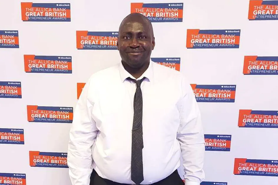Victor Ajabo yn gwenu ar y camera, yn erbyn cefndir yn arddangos logo Gwobrau Entrepreneur