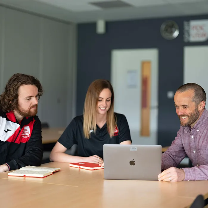 Two research students and lecturer sitting at a table looking at a laptop