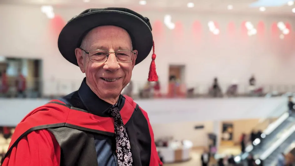 A man smiling wearing a black and red graduation gown and hat