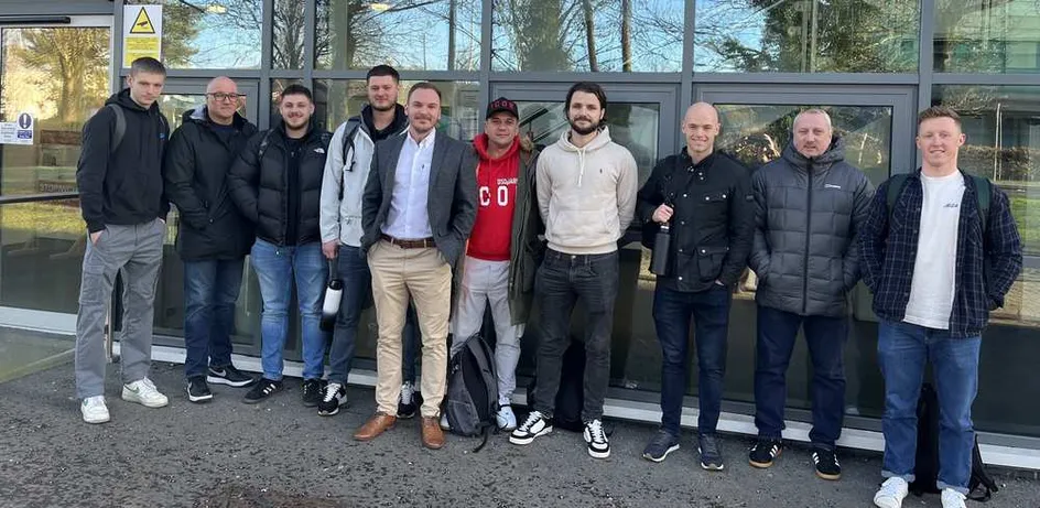 Grŵp o ddynion yn sefyll mewn llinell o flaen adeilad