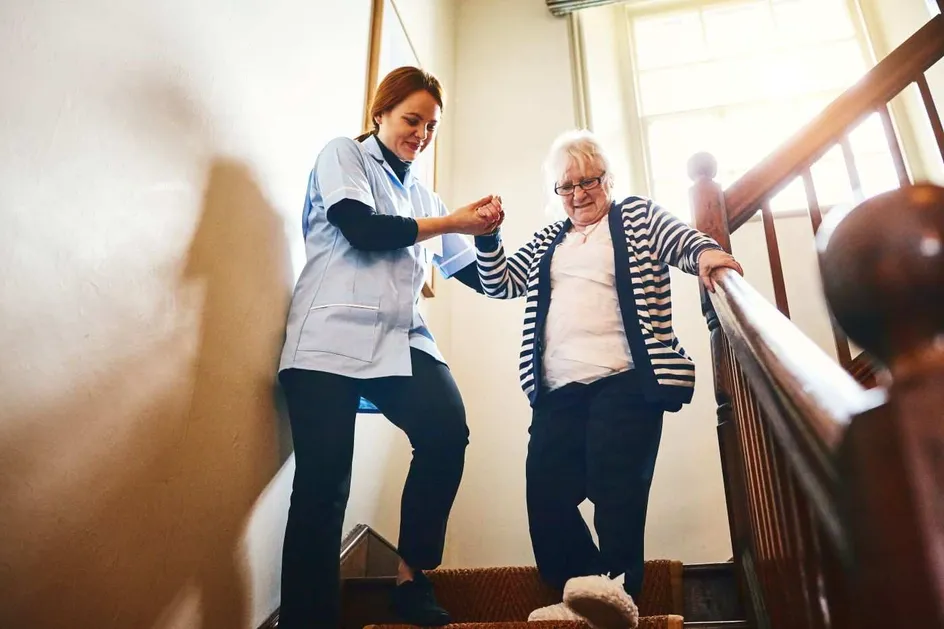 A carer helping an elderly lady down some stairs