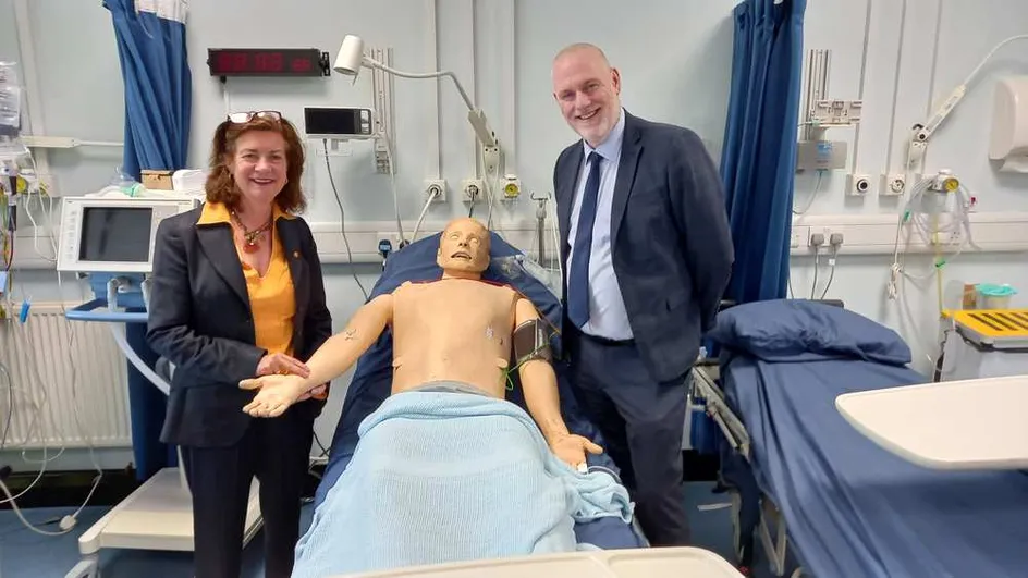 Two individuals (Eluned Morgan on the left and Ben Calvert on the right) standing beside a mannequin in a hospital setting.