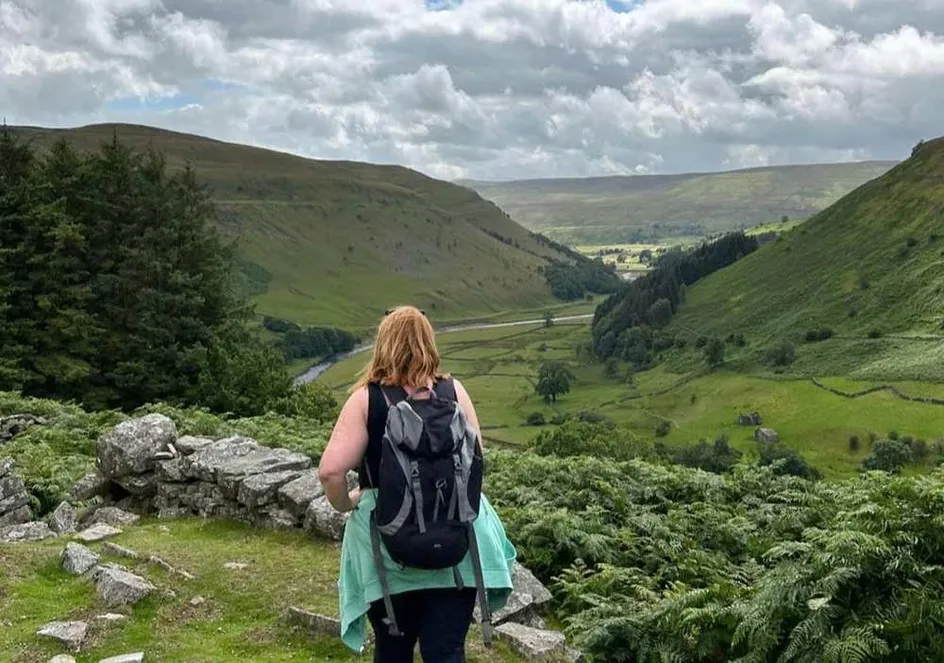 A woman with a backpack standing at the edge of a valley, gazing into the distance.