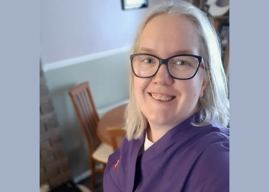 Myfyrwraig nyrsio Sinead Harris yn gwenu yn ei sgrybiau porffor