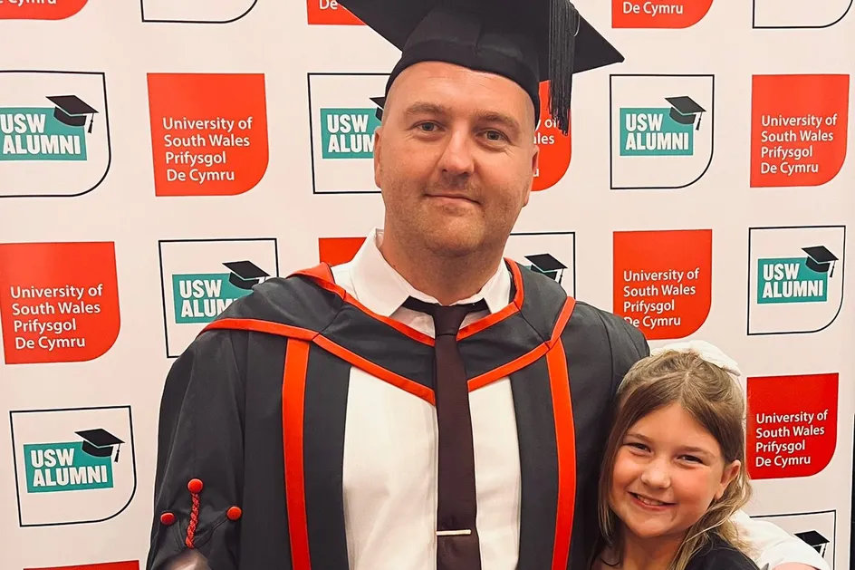 Mae Lewis yn sefyll gyda'i fraich o amgylch ei ferch. Mae hi'n gwenu ac yn dal tedi arth.