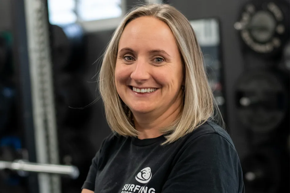Joanna is stood with arms crossed and smiling at the camera. She is wearing a black t-shirt with the 'Surfing Australia' logo on.