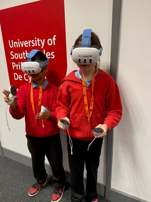 Dau blentyn ysgol yn defnyddio'r clustffonau VR a setiau llaw o Goggleminds