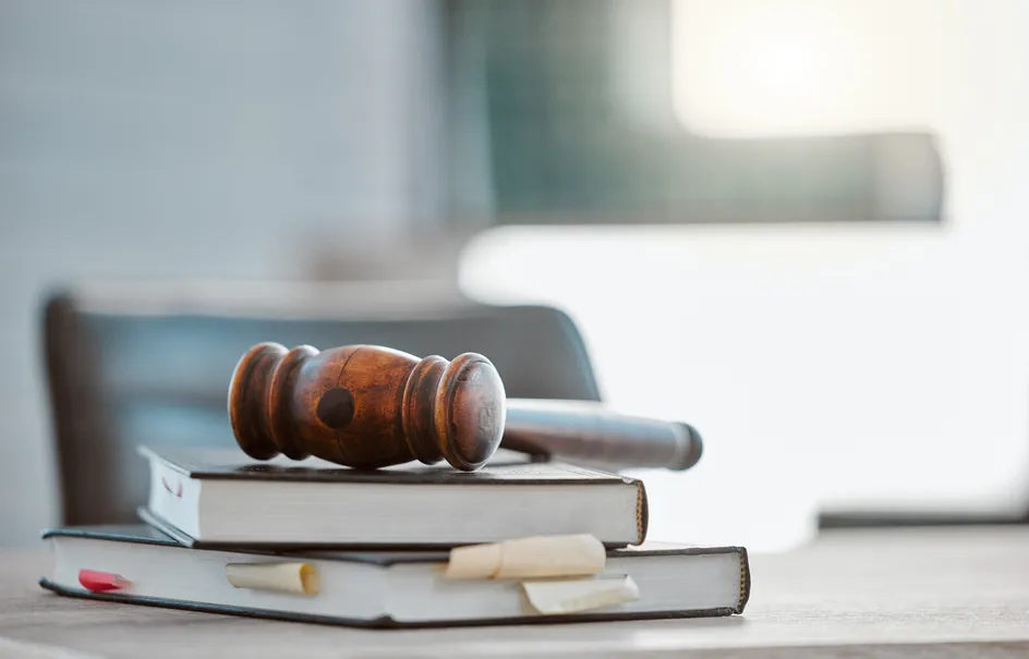 A wooden judge's gavel resting on top of two stacked hardcover books with bookmarks and sticky notes.