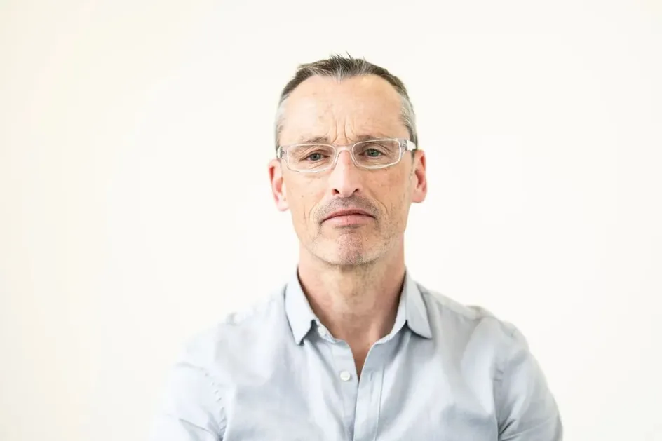 A man with short grey hair, glasses, and light skin.