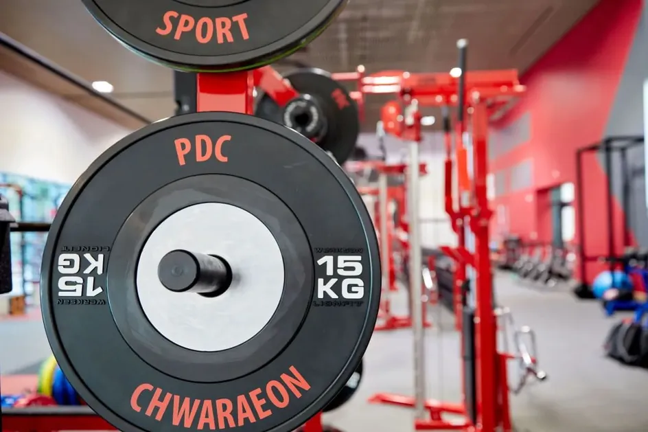 Llun agos o blât pwysau du 10kg wedi'i labelu “PDC Chwaraeon” ar rac codi pwysau coch a du.