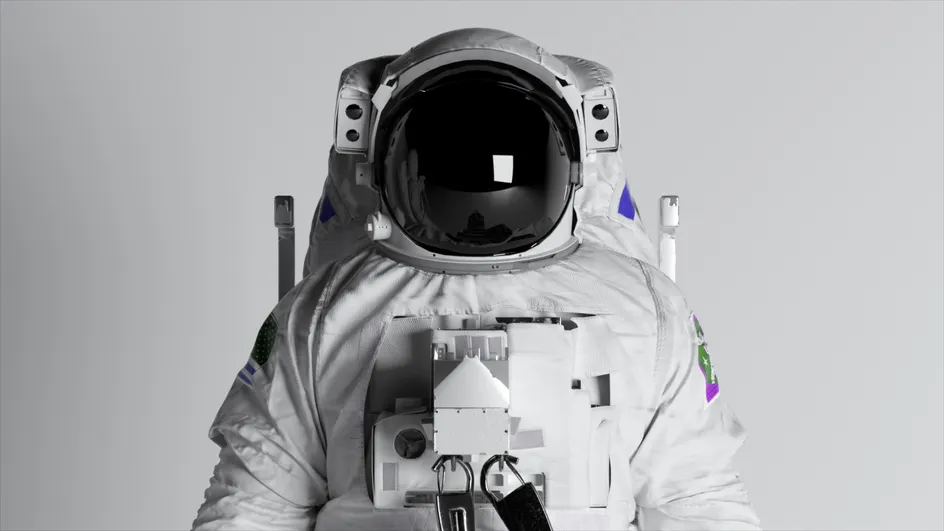 Front-facing view of an astronaut in a white spacesuit against a plain light-grey background. The helmet visor is black and reflective.