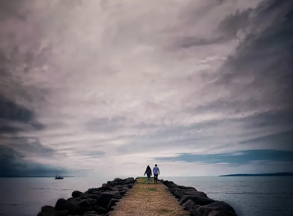 Dau berson yn cerdded ar hyd pier ger y môr