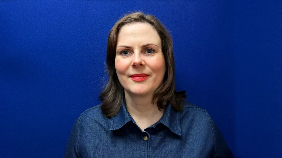 An image of a woman with long dark hair. She is wearing a blue blouse and smiling for the camera.