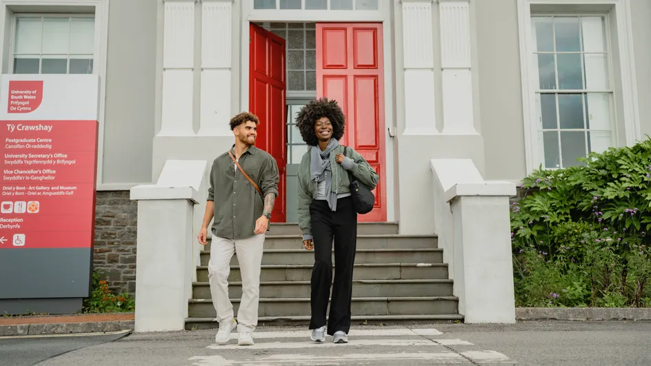 Two people walking down the front steps on campus.