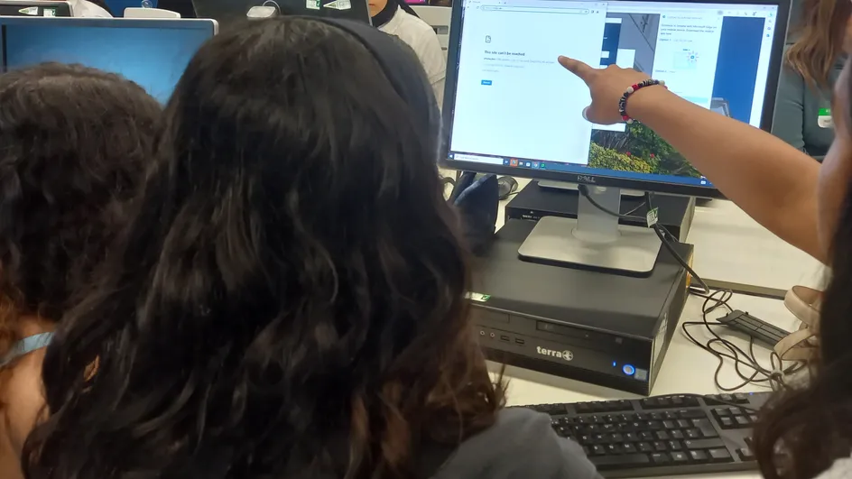 Three students looking at a computer screen, with one pointing to some coding shown on the screen.