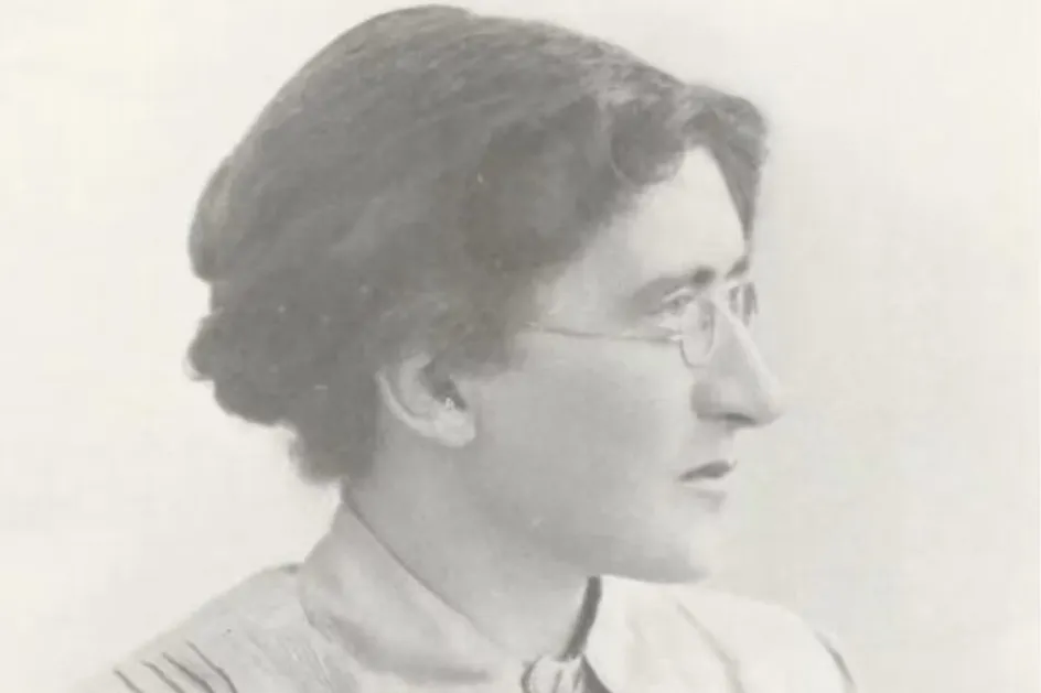 An old photographic portrait of a woman. She is wearing glasses and has long hair that is pinned up.