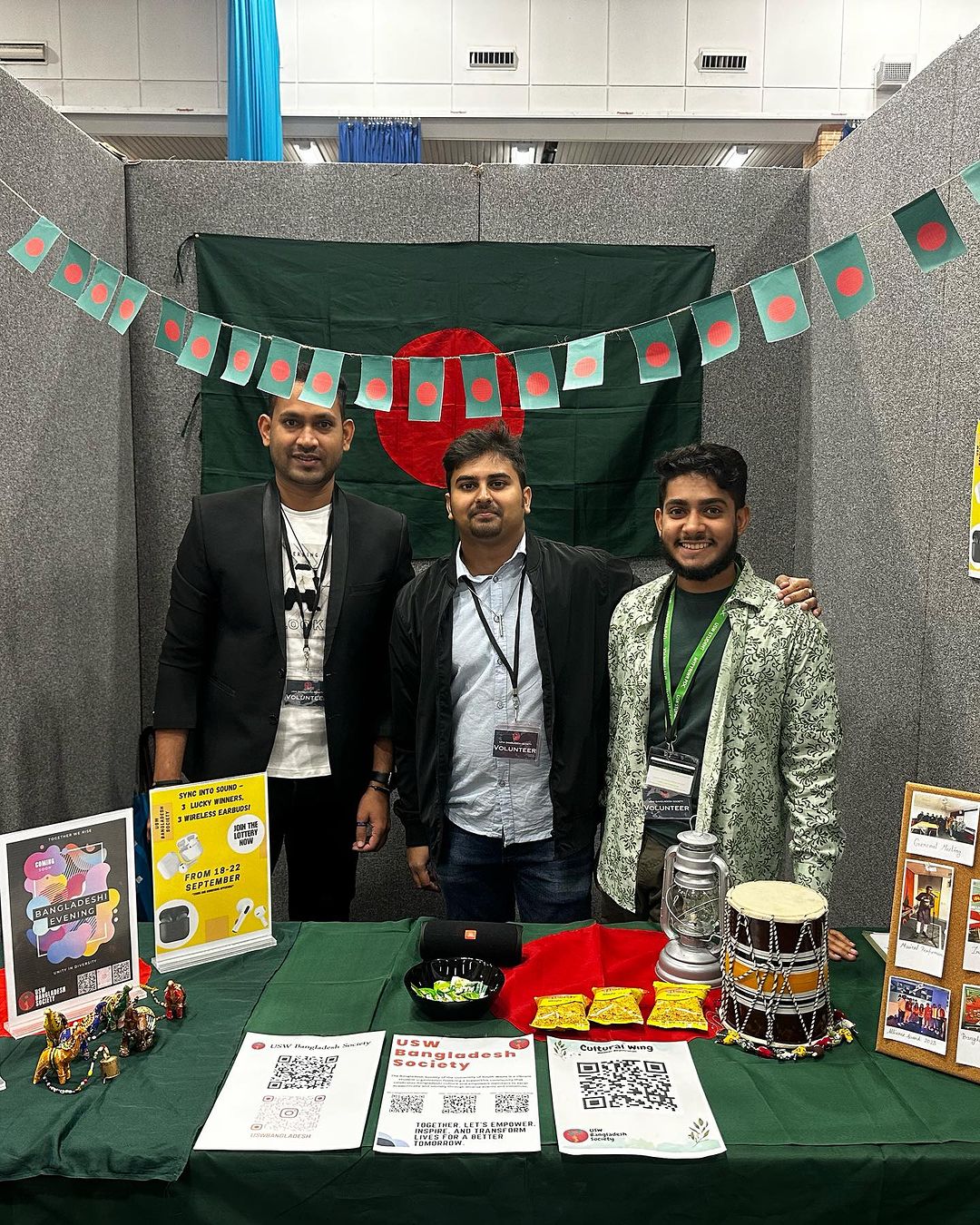 3 members of the Bangladesh society smiling at the camera at USW Fresher's fair, surrounded by Bangladesh flags