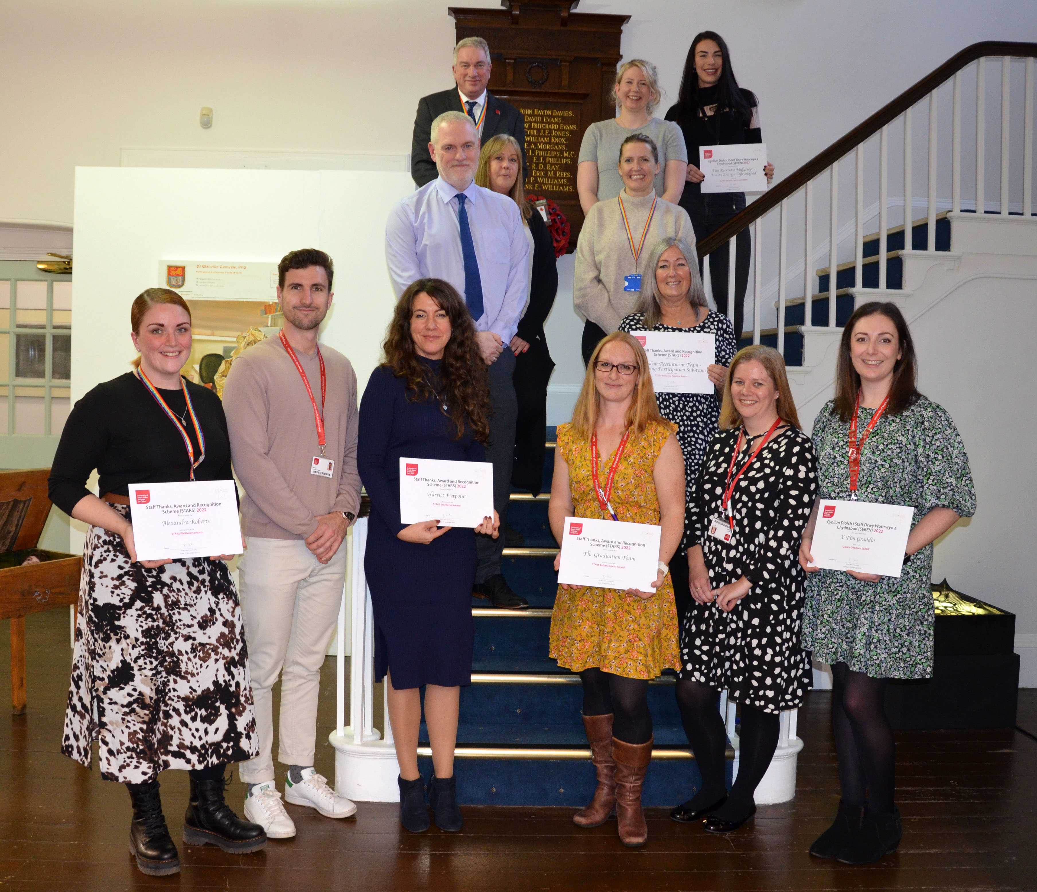 A group of staff that have been recognised for an award are smiling with their certificates.