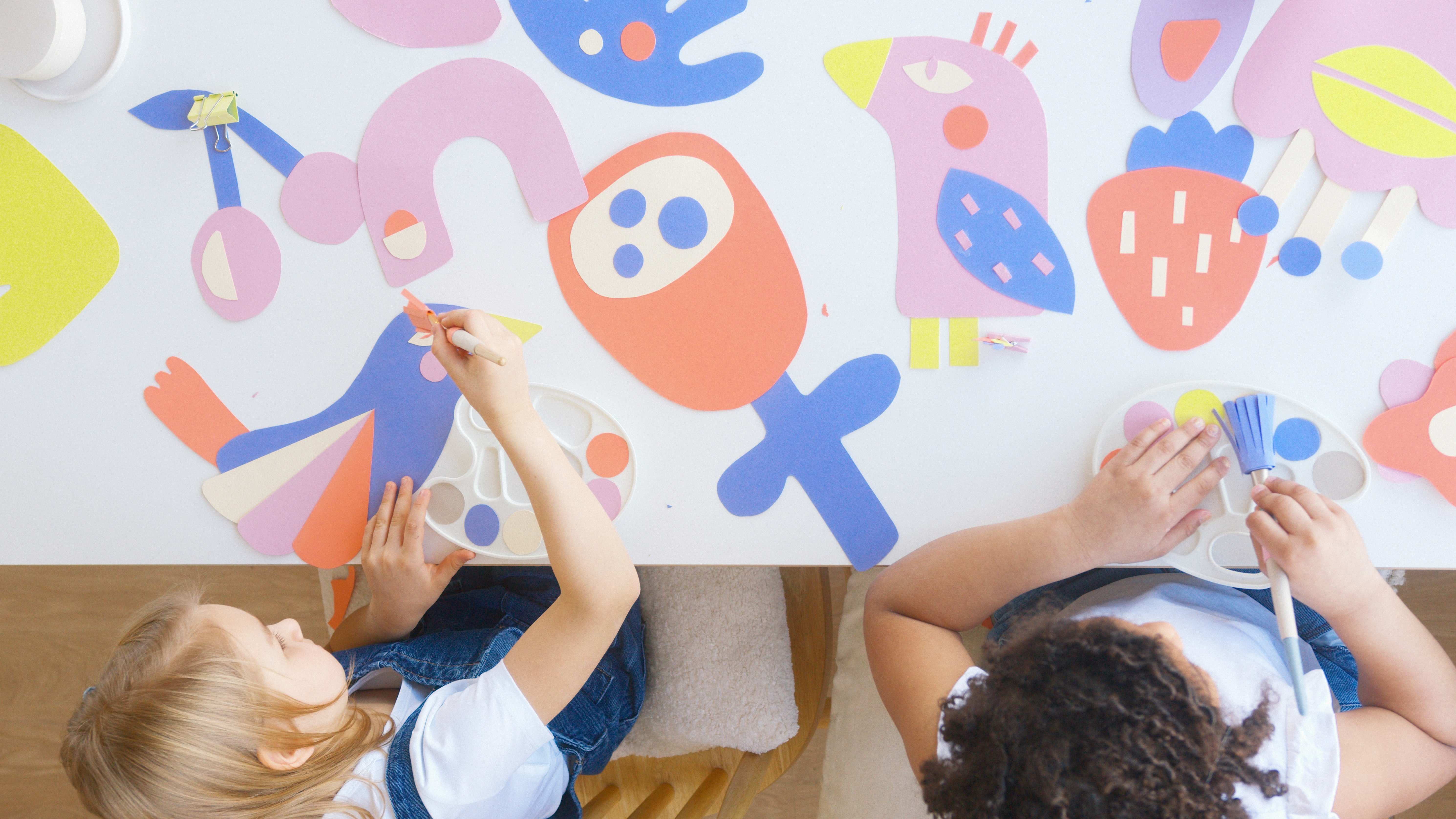 two children sitting at a table painting a picture