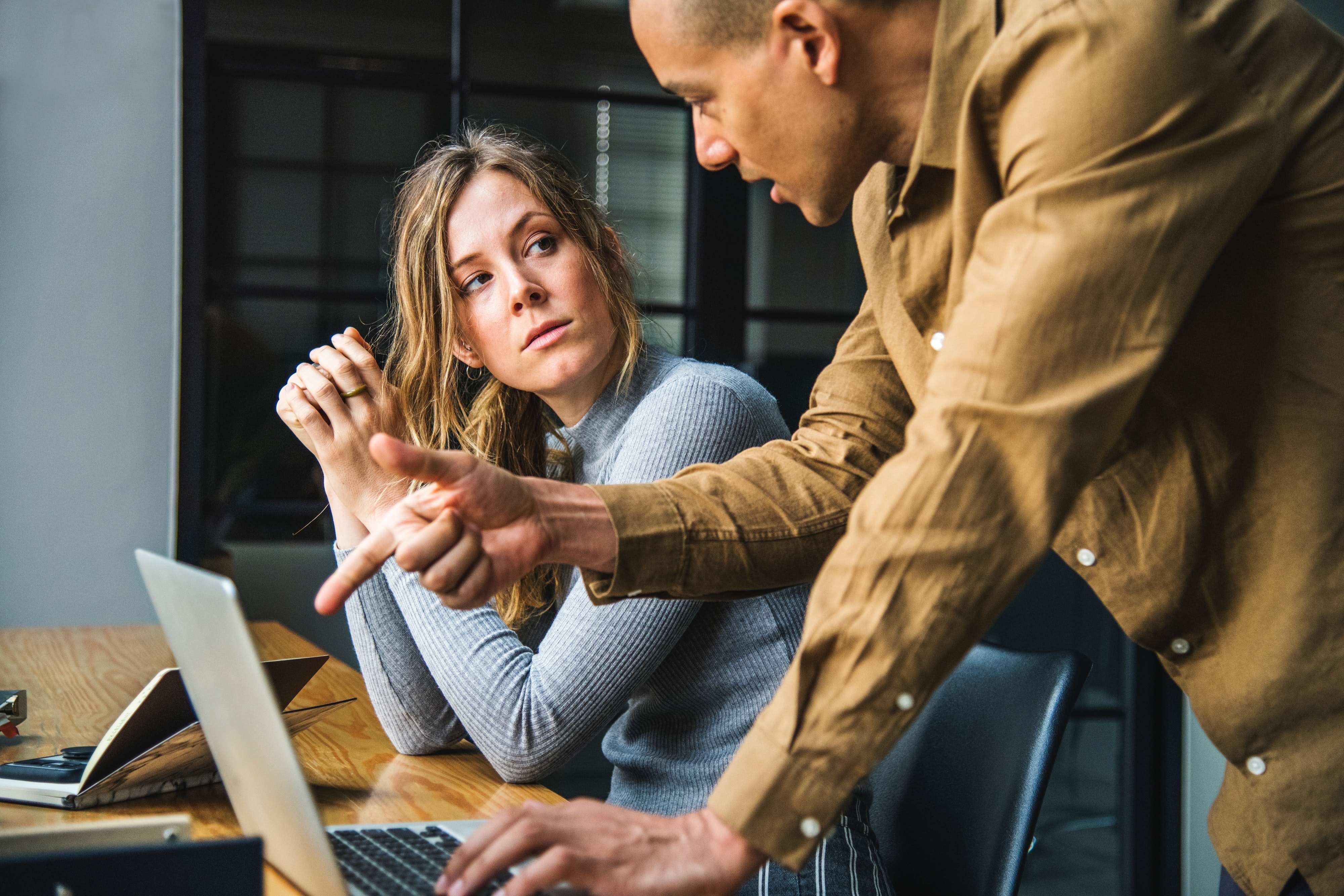 two people having a conversation at a desk with a laptop