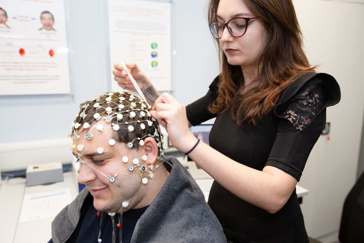 A student applies an EEG to another student's scalp to measure the electrical activity in their brain in a psychology laboratory