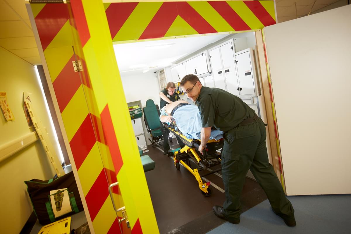 Two paramedics wheeling in simulated patient into the ambulance simulator in the clinical simulation centre