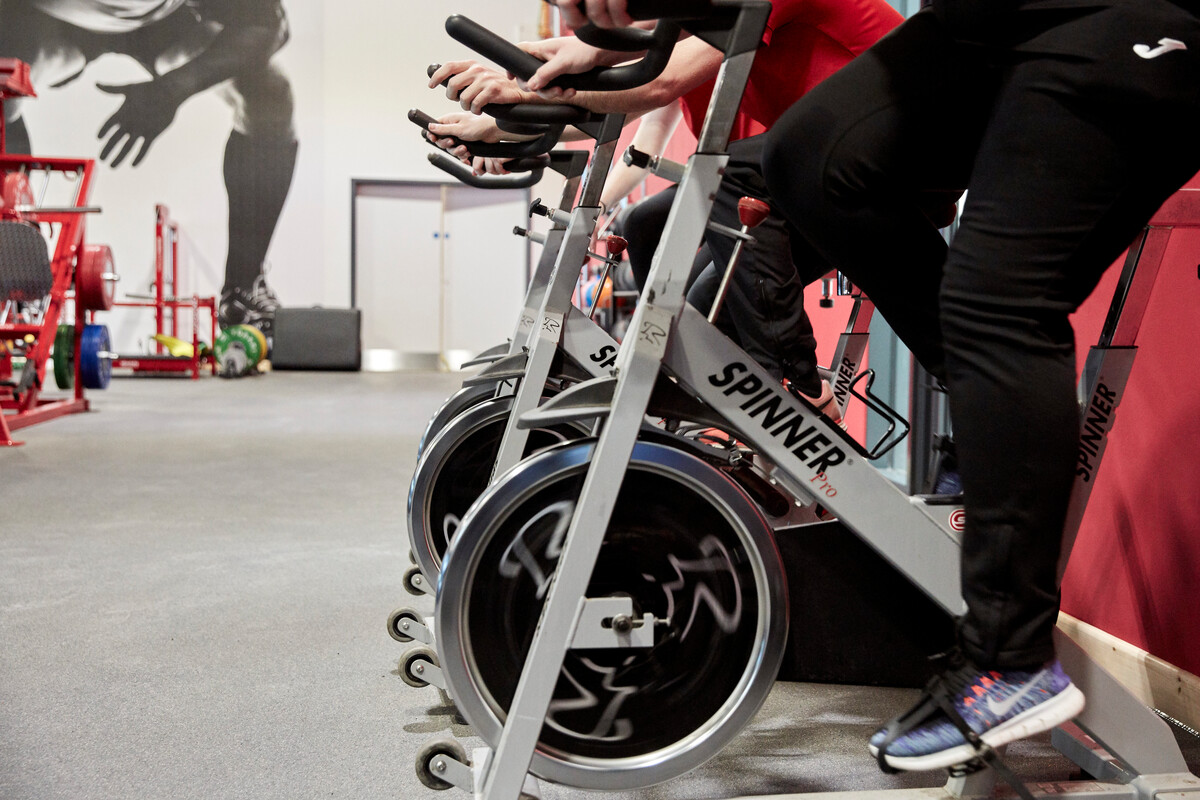 A group of students working out on a row of exercise spin bikes.