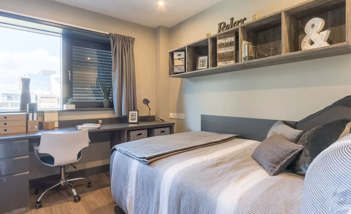 Overview photo of a cluster room at Lumis. There is a bed, shelves and a desk area overlooking the window
