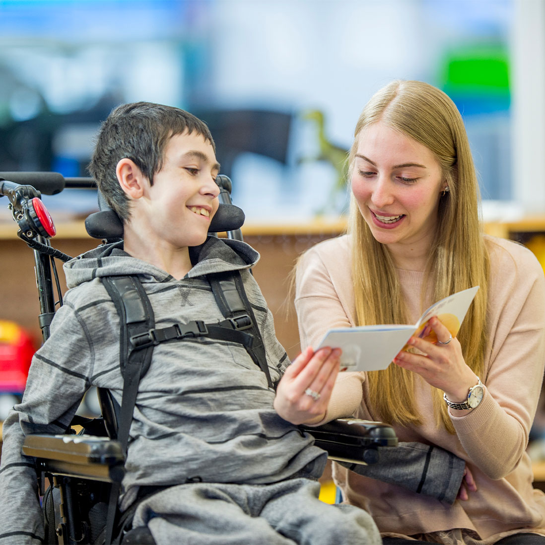Learning and support worker reading a book to a child sitting in a wheelchair