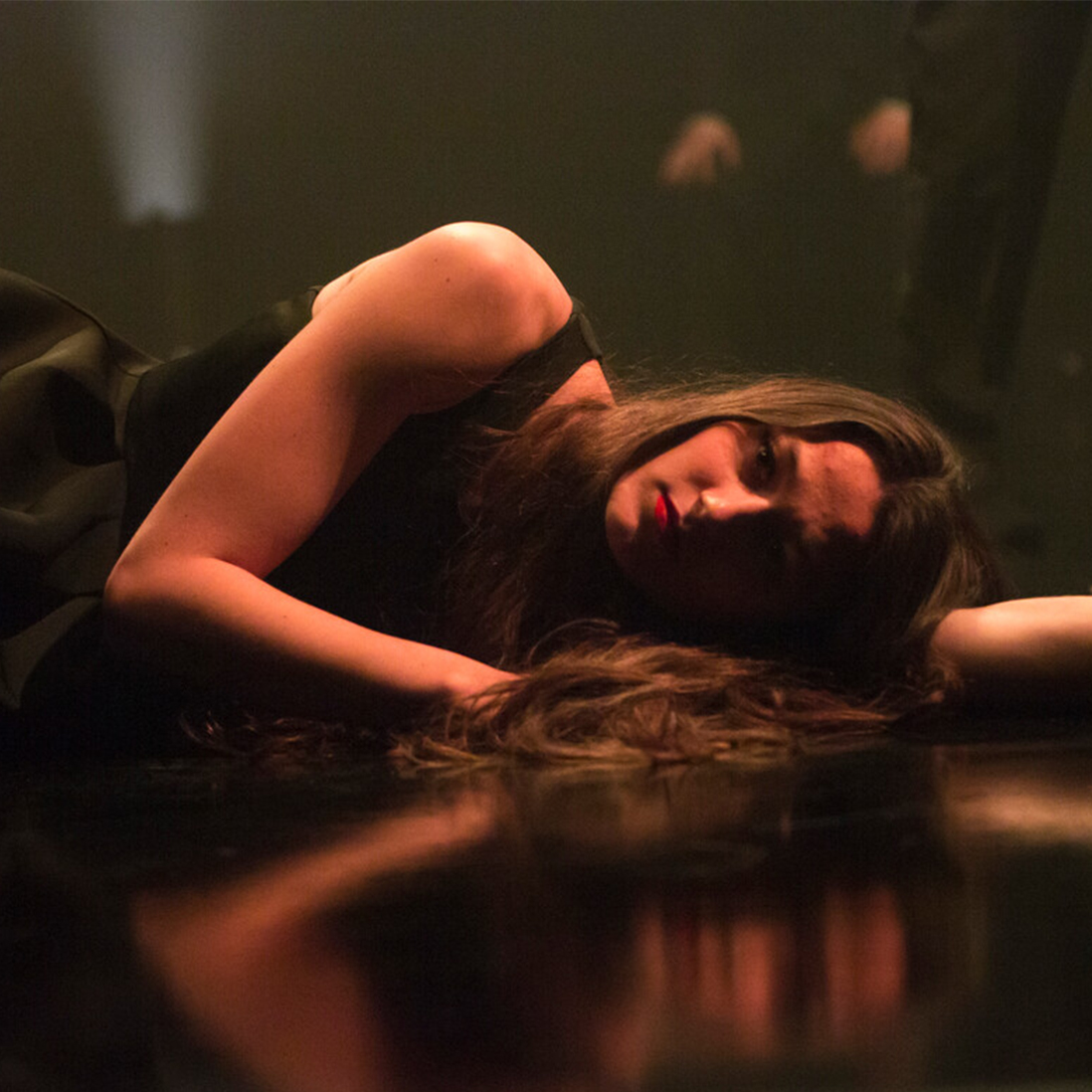A dramatically lit student laying down on their side staring intensely at the camera