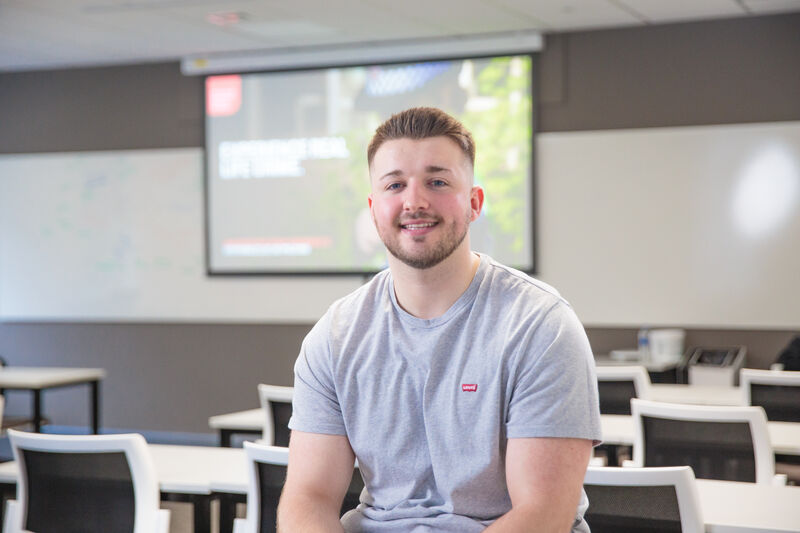 An image of a policing student sat in a classroom and smiling at the camera.