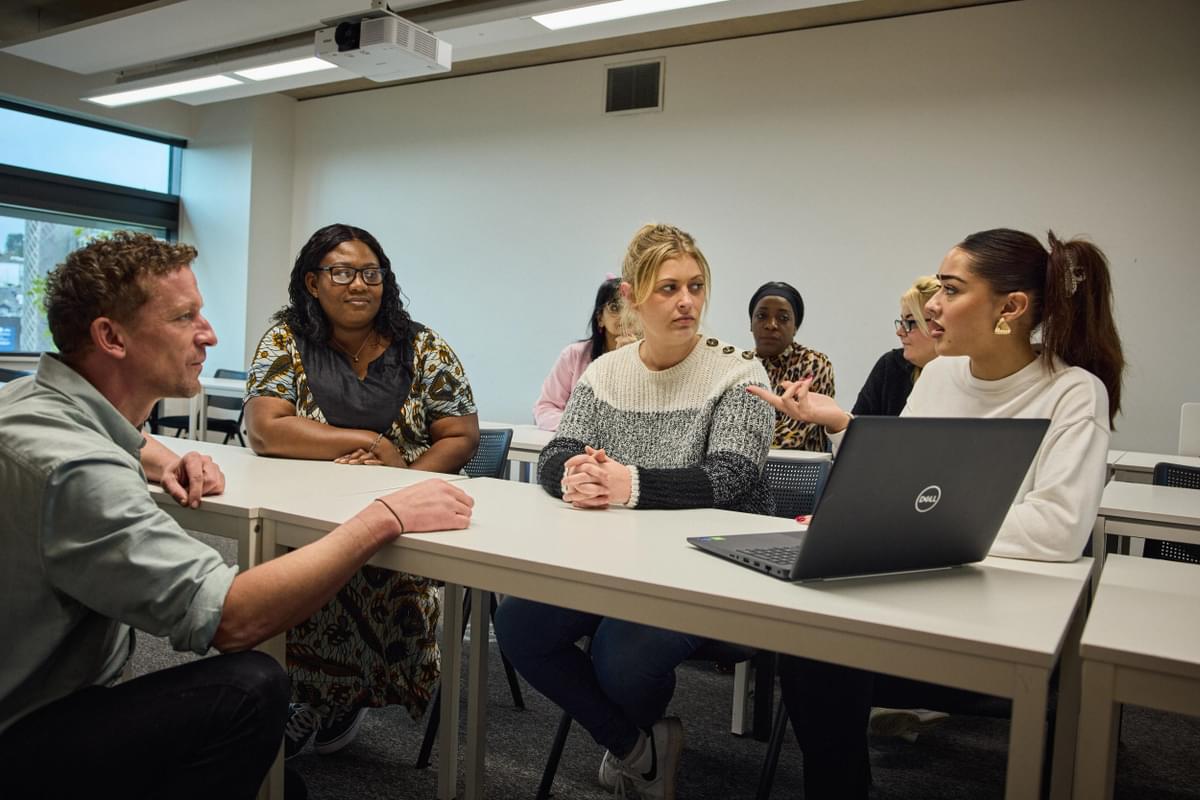three social work students sitting at a desk involved in disucssion with the course lecturer who is sitting with them