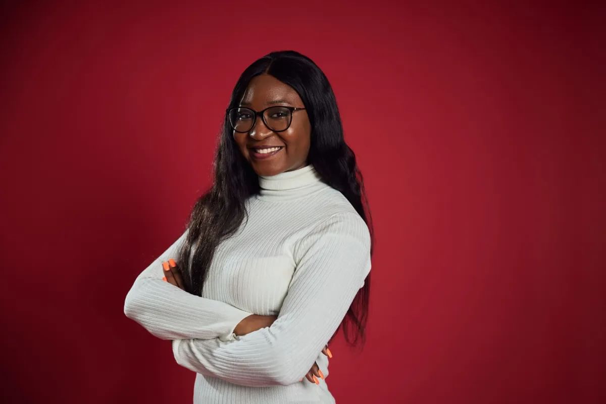 Accounting student Joelle, smiles at camera with her arms crossed, in front of a red backdrop